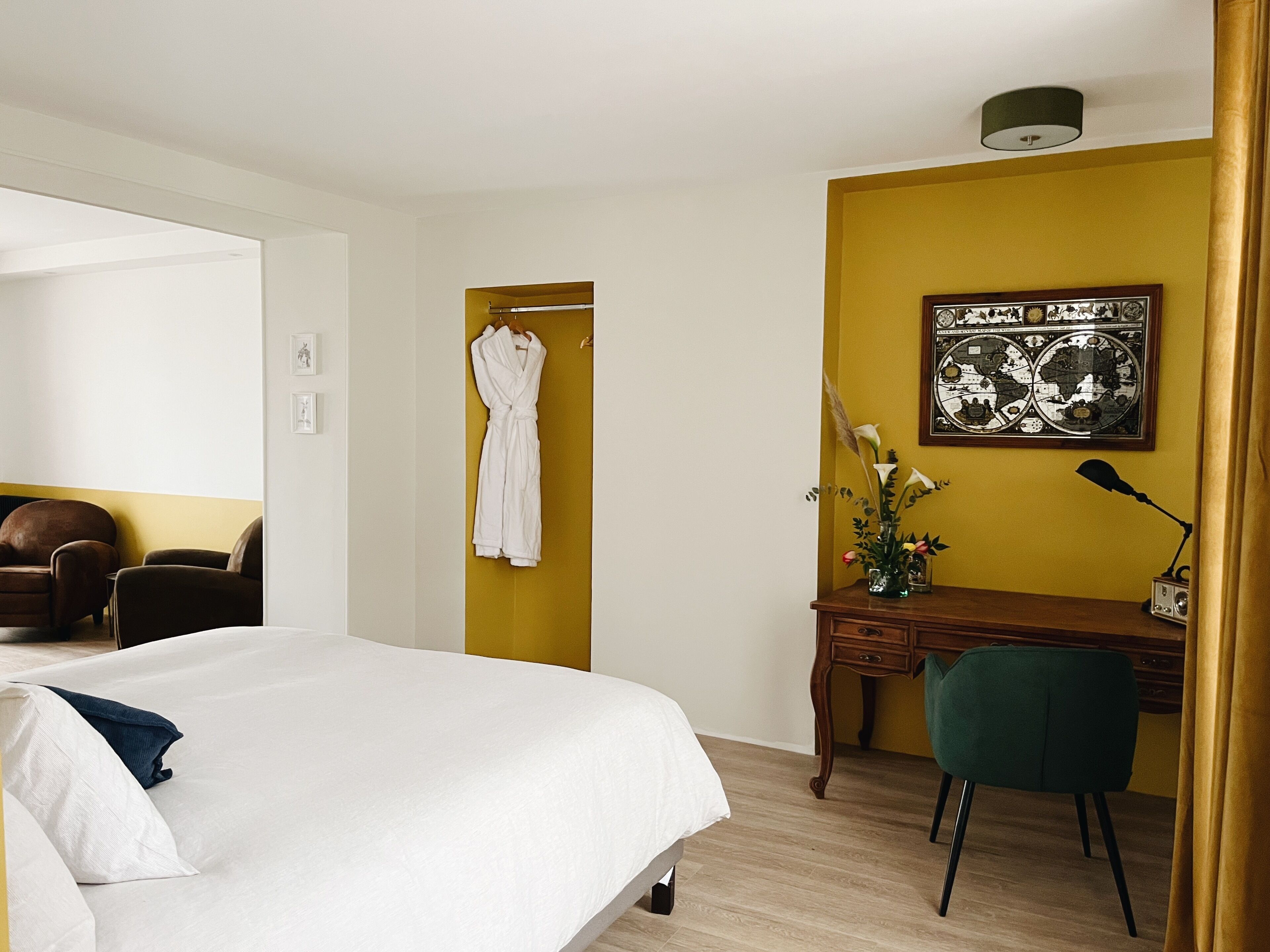 Una habitación de hotel con una cama, un escritorio, una silla, una bata colgada en la pared y un cuadro enmarcado.