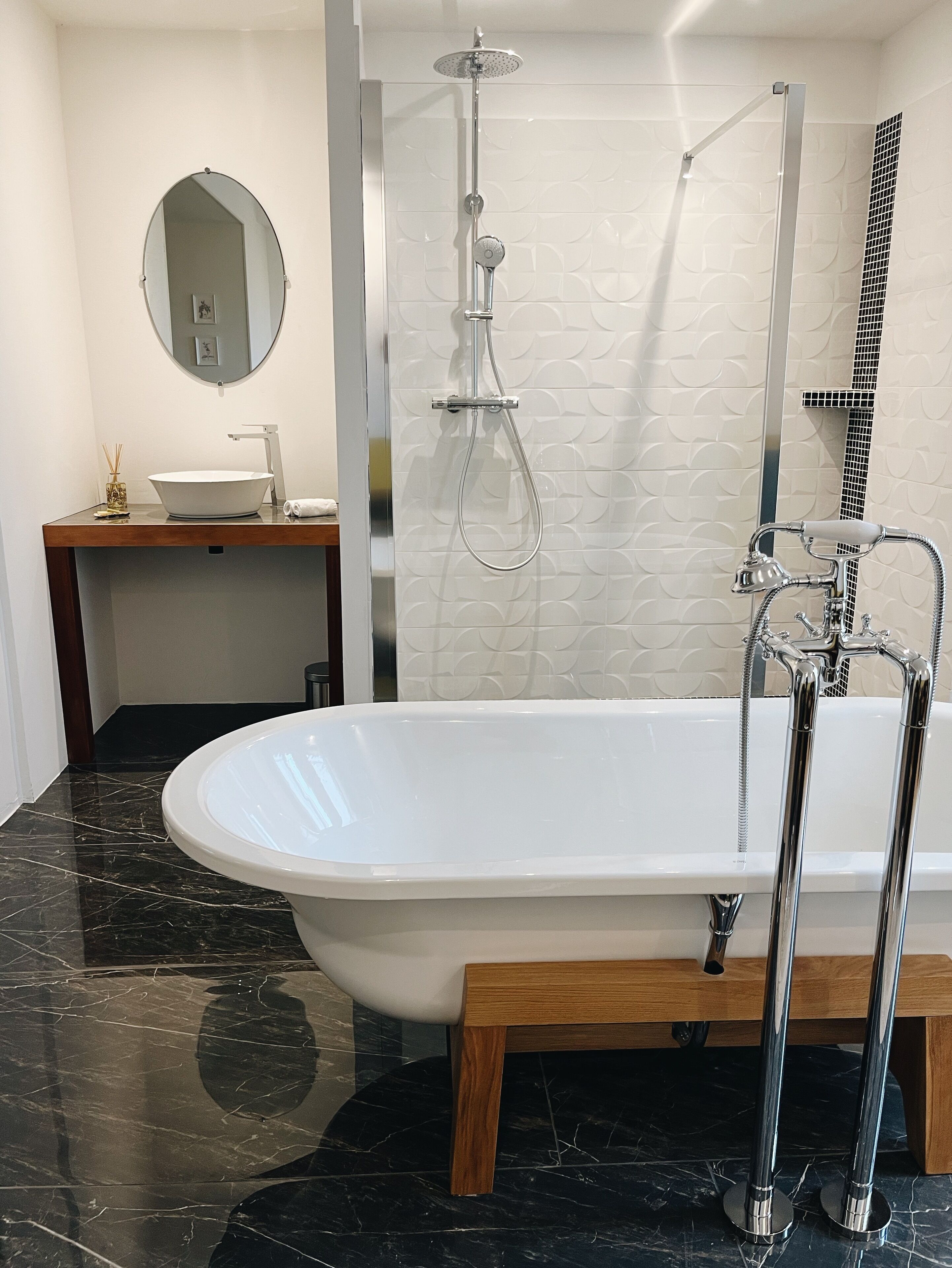 A modern bathroom with a freestanding bathtub, a shower with a handheld showerhead, a round mirror, and a vanity with a sink and decorative items.
