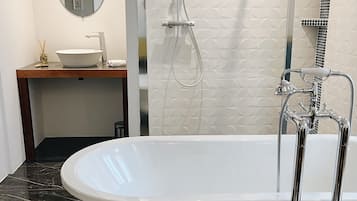 A modern bathroom with a freestanding bathtub, a shower with a handheld showerhead, a round mirror, and a vanity with a sink and decorative items.