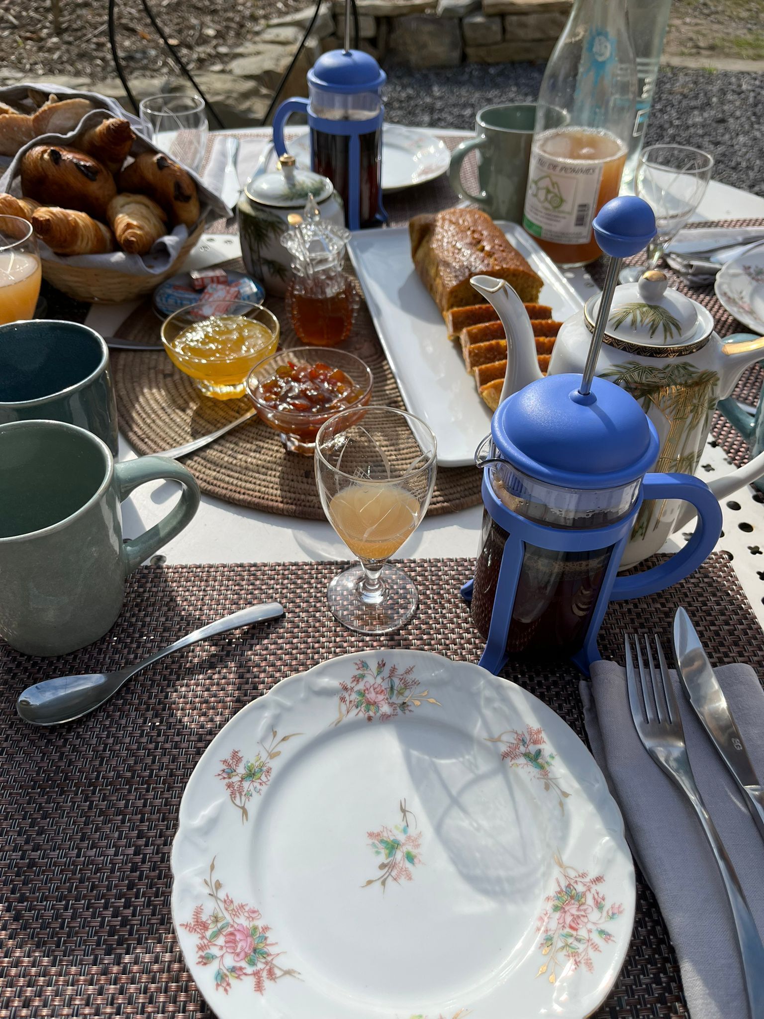 A table set with croissants, a coffee pot, a teapot, a glass of juice, and a plate of food.