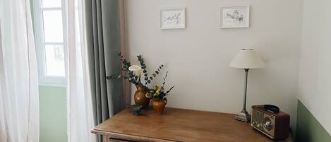A room with a wooden desk, a lamp, a radio, and framed botanical prints on the wall.