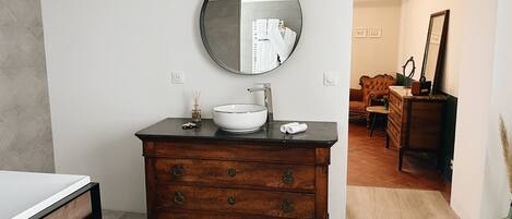 A bathroom with a round mirror, a white sink, and a wooden vanity with drawers.