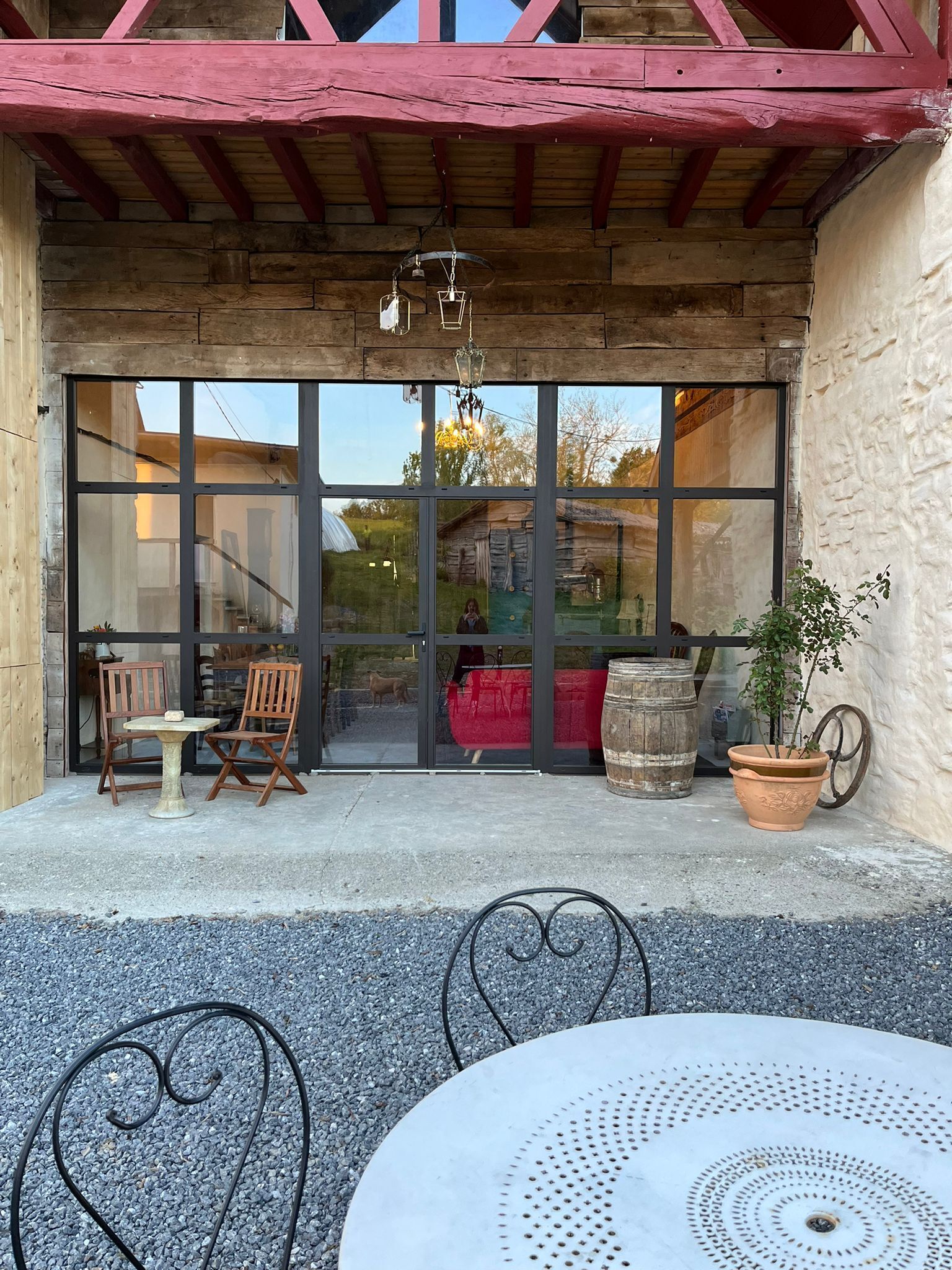 A rustic wooden building with a large glass door, a small outdoor seating area with a table and chairs, and a potted plant.