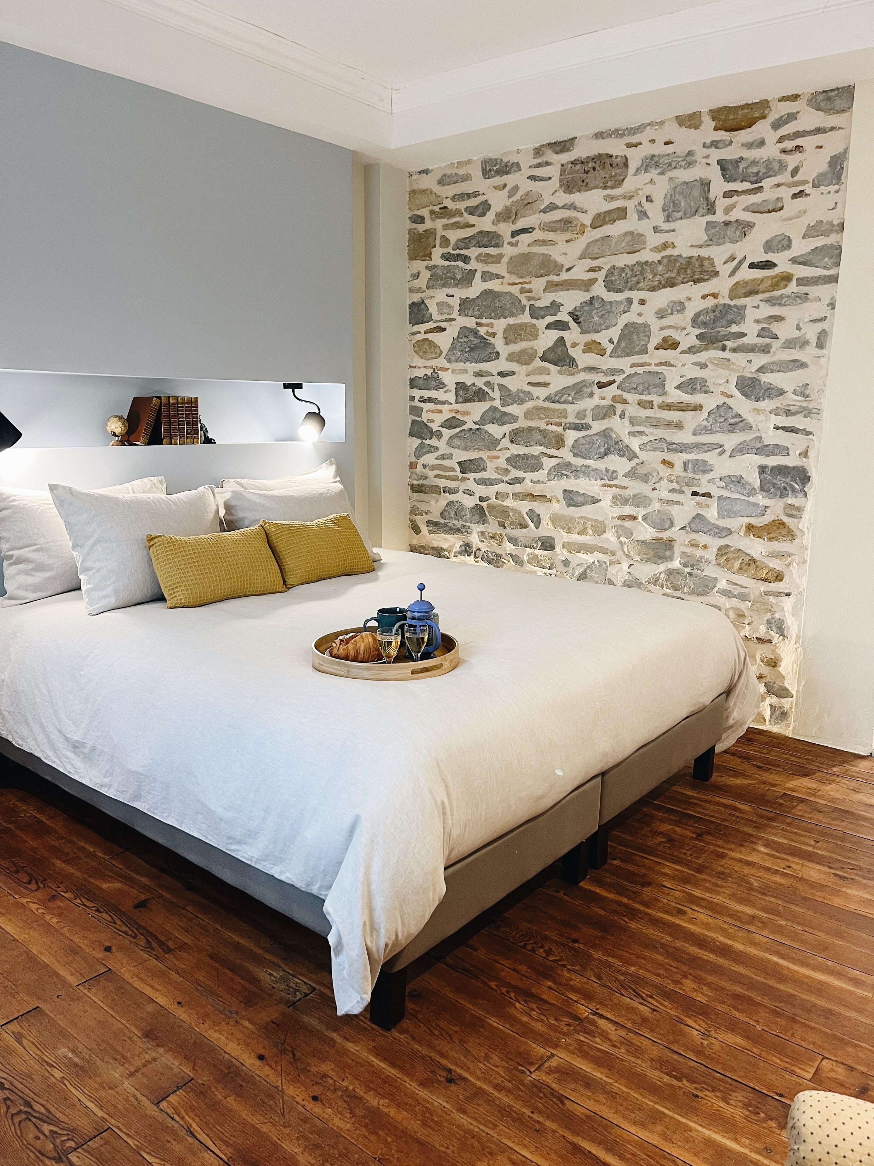 A bedroom with a stone wall, a bed with white bedding, and a tray with breakfast items.