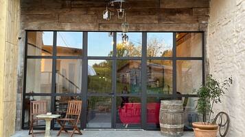Un bâtiment rustique en bois, doté d’une grande porte vitrée, de chaises en bois, d’une petite table et d’une plante en pot à l’extérieur.
