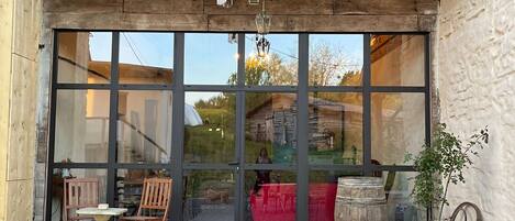 A rustic wooden building with a large glass door, wooden chairs, a small table, and a potted plant outside.