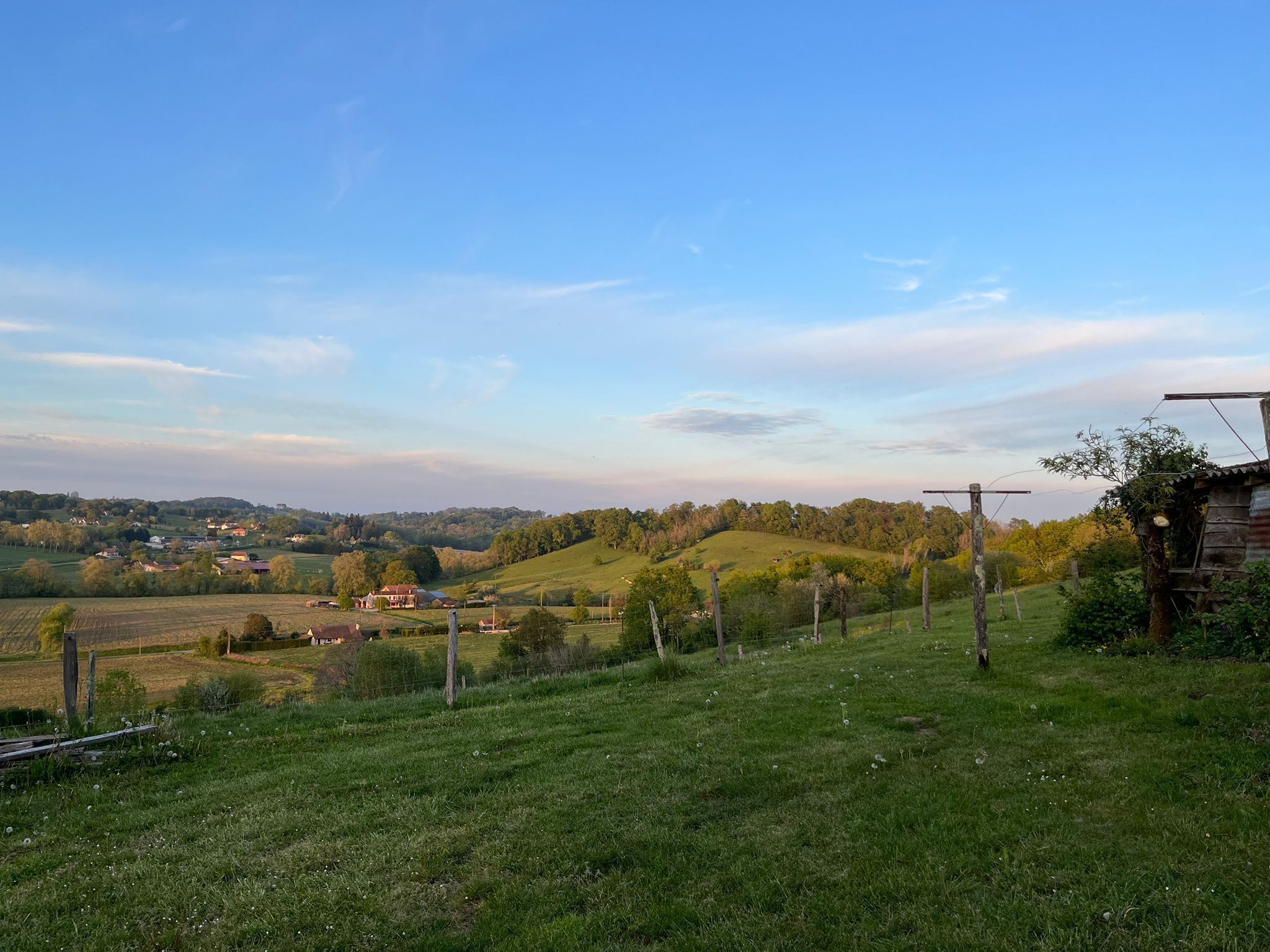 A rural landscape with rolling hills, a wooden fence, and a small house.