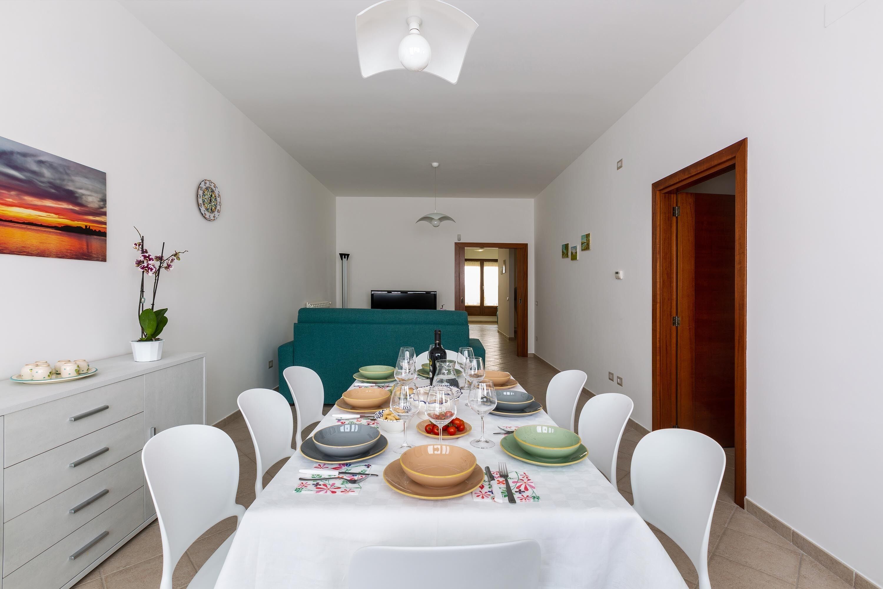 A dining area with a table set for four, chairs, a sofa, and a TV in the background.