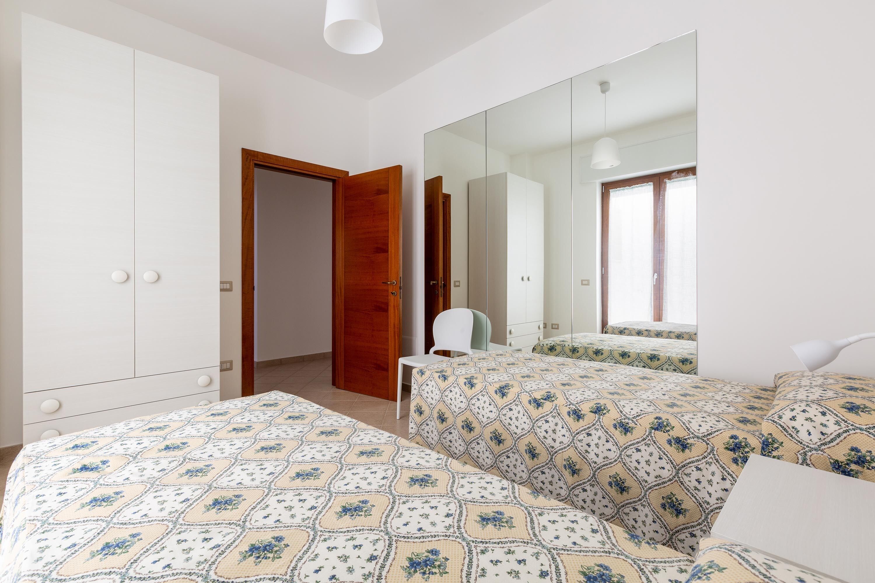 A bedroom with a bed, a chair, a wardrobe, and a mirror.
