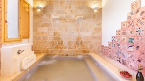 A bathroom with a bathtub, a wooden door, a sink, and a wall with decorative tiles. - Trullo Sorrentino Luxury by Perle di Puglia (Ostuni)