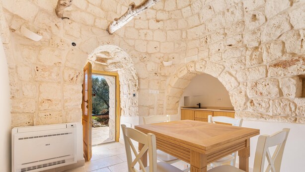 A room with a stone wall, a wooden table, and white chairs. - Trullo Sorrentino Luxury by Perle di Puglia (Ostuni)