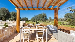 An outdoor patio with a wooden pergola, white chairs, and a dining table. - Trullo Sorrentino Luxury by Perle di Puglia (Ostuni)