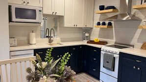 A modern kitchen with white upper cabinets, dark lower cabinets, a microwave, stove, and a sink.
