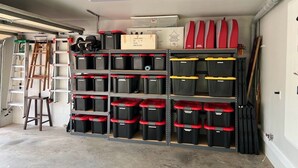 A garage with shelves of storage bins, a ladder, and a workbench.