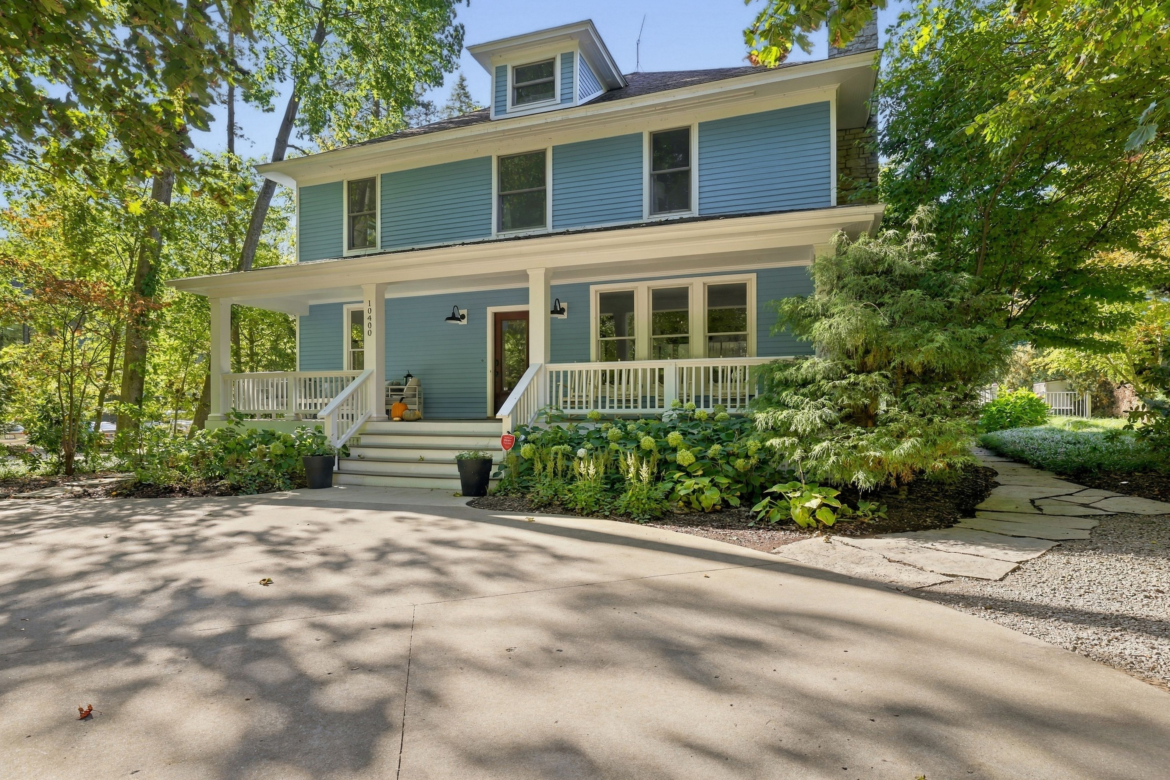 A two-story house with a front porch, a driveway, and surrounding greenery.