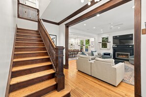 A wooden staircase leading to a living room with a fireplace, a sofa, and a television. - 2027 OPEN! Union Pier Home With Pool and Hot Tub! Close To Private Beach! (Union Pier)