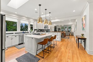 A modern kitchen with white cabinetry, a central island, bar stools, and pendant lighting. - 2027 OPEN! Union Pier Home With Pool and Hot Tub! Close To Private Beach! (Union Pier)