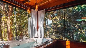 Un baño moderno con una bañera grande, techo de madera y ventanas amplias que dan a árboles y follaje.