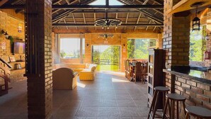 Amplio espacio interior con techo alto, paredes de ladrillo y un gran ventanal que permite la entrada de luz natural. Hay zonas de estar con mesas y sillas, además de una barra con taburetes.