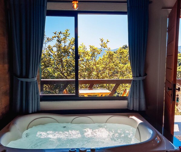 A hot tub with a view of trees and a wooden deck outside.