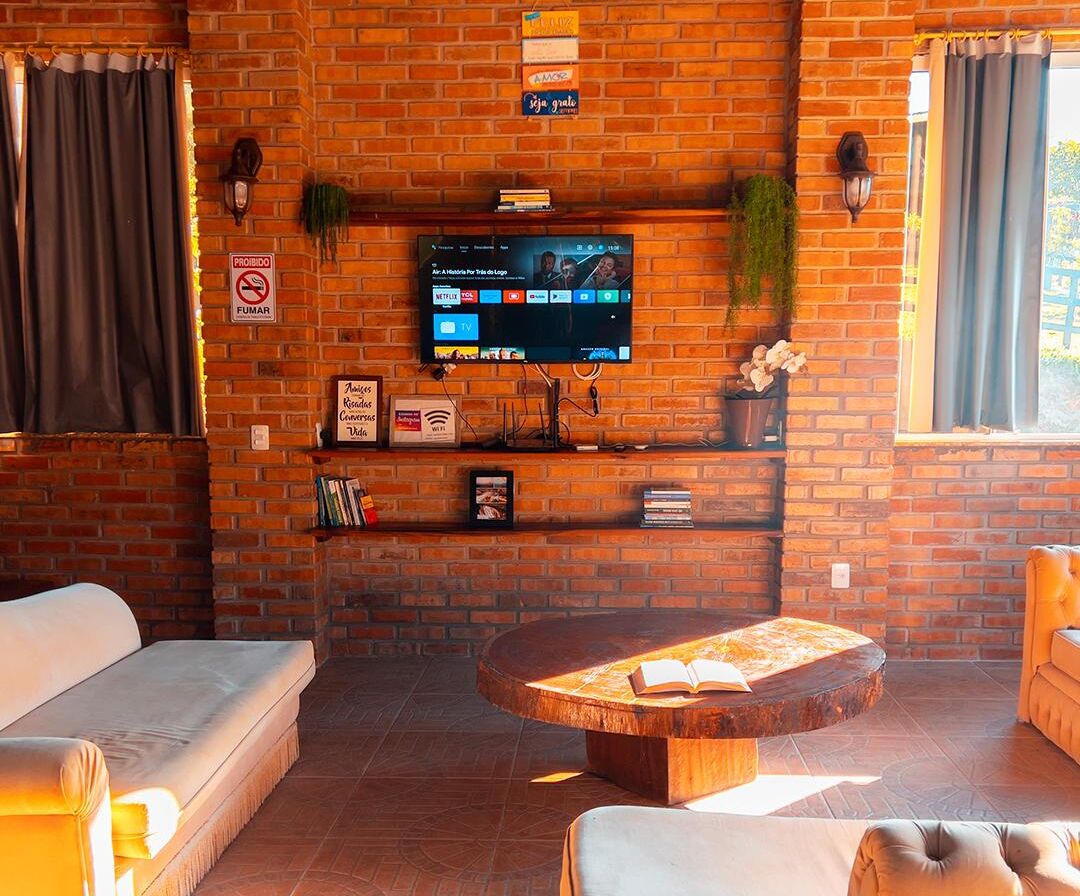 Ein gemütliches Zimmer mit Backsteinwand, einem flachbildfernseher, der über einem Regal angebracht ist, einem runden Holztisch und zwei Sofas.