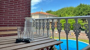 Una terraza de madera con una mesa de vidrio, barandilla de metal y una piscina al fondo.