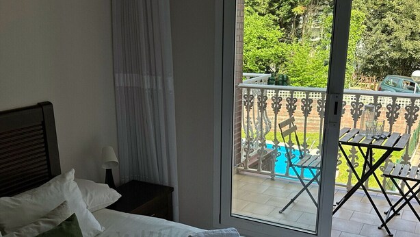 Habitación de hotel con cama, ventana con vista a una piscina y mobiliario exterior.
