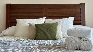 Una cama bien hecha con una colcha estampada, una variedad de almohadas y toallas blancas enrolladas.