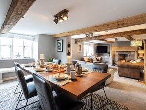 A spacious living area with a wooden dining table set for a meal, a fireplace, and a cozy seating area with a sofa and chairs. - Longlands Farm Cottage (Grange-over-Sands)