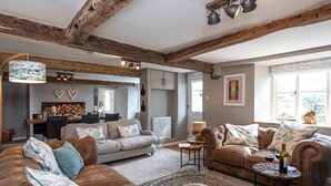 A cozy living room with a brown leather sofa, a patterned rug, and a dining area with a wooden table and chairs. - Longlands Farm Cottage (Grange-over-Sands)