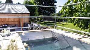 A swimming pool with a metal safety railing, a wooden deck, and a stone wall in the background. - Longlands Farm Cottage (Grange-over-Sands)