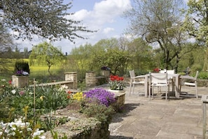 A garden patio with stone flooring, a table and chairs, and various flowering plants. - The Old Manor House  (Shipston on Stour)