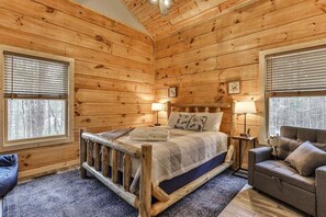 Ein Schlafzimmer in einer Holzhütte mit einem Bett, zwei Nachttischlampen, einer Holzbank und einem Sofa.