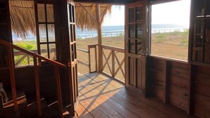 Een houten hut met een houten trap die leidt naar een balkon met uitzicht op een strand.