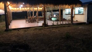 An outdoor dining area with a thatched roof, wooden tables, and chairs.
