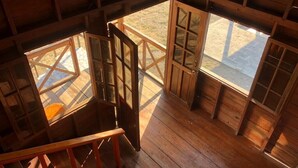 A wooden interior with a staircase, a wooden door, and a view through a window.