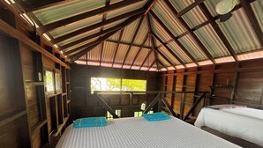 A room with a high ceiling, wooden walls, and a metal roof. There are two beds with white and patterned bedding, and a blue towel on the bed.