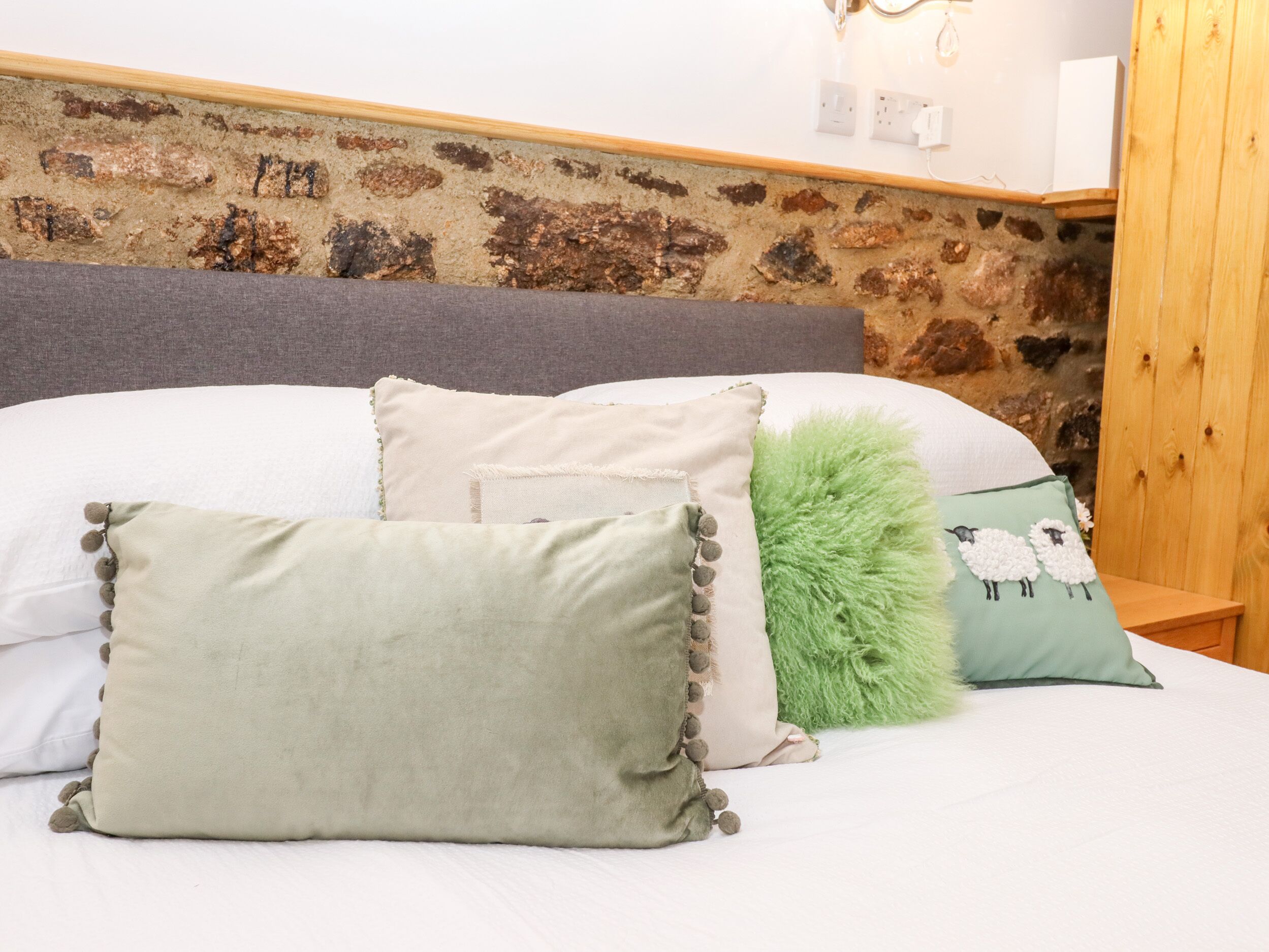 Una cama con varias almohadas y una pared de piedra al fondo.
