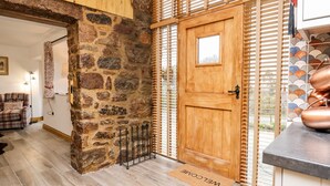 Un interior rústico con pared de piedra, puerta de madera y felpudo que dice 'Welcome'.
