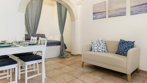 A dining area with a table set for four, a sofa, and a window with curtains. - Cozy Historic Home by Wonderful Italy (Ostuni)