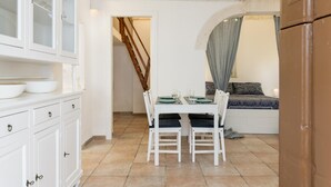 A compact kitchen with white cabinetry, a dining table with chairs, and a bed with a grey canopy. - Cozy Historic Home by Wonderful Italy (Ostuni)