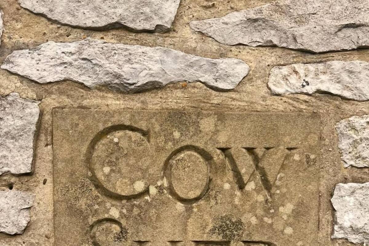A stone wall with a carved sign that reads "COW SHED."