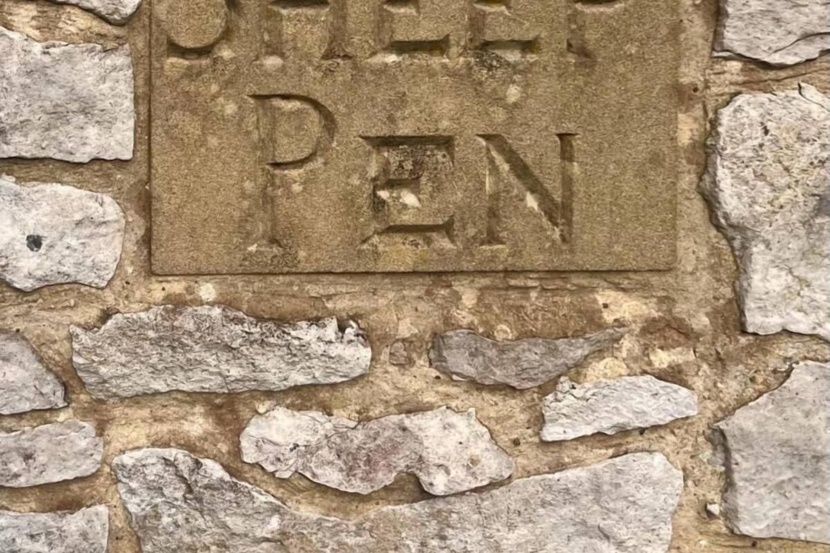 A stone wall with a plaque that reads "Sheep Pen."