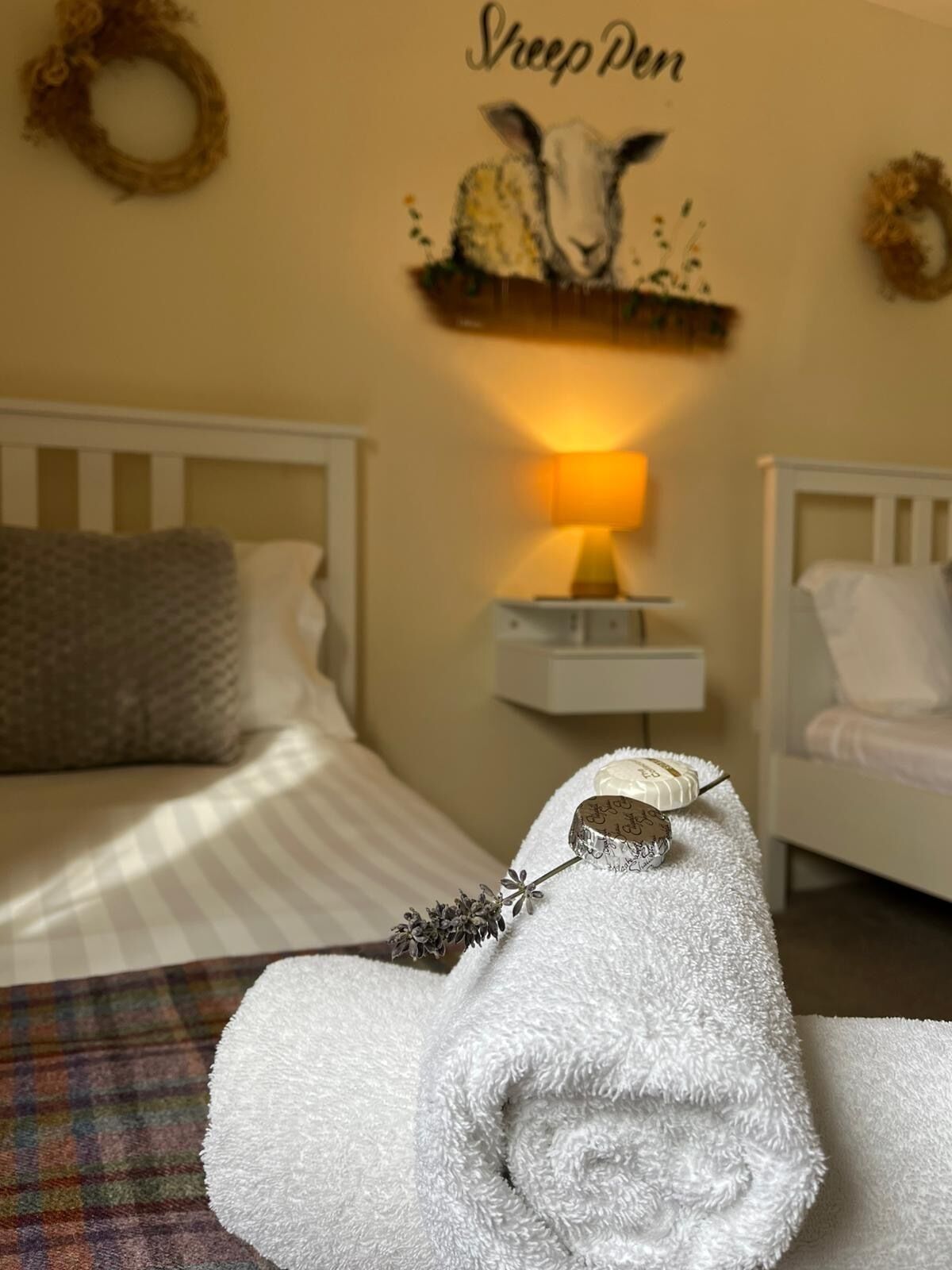 A cozy bedroom with a bed, a bedside table with a lamp, and a wall decoration of sheep.