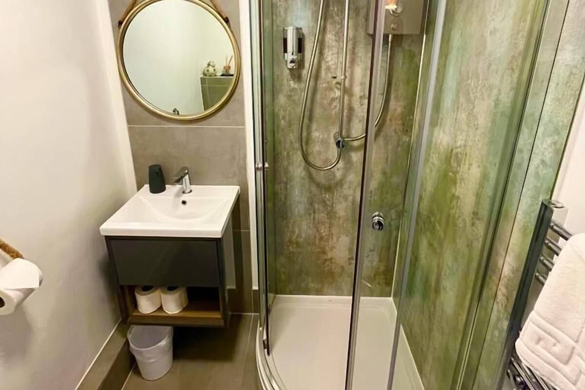 A modern bathroom with a glass-enclosed shower, a round mirror, and a white sink.