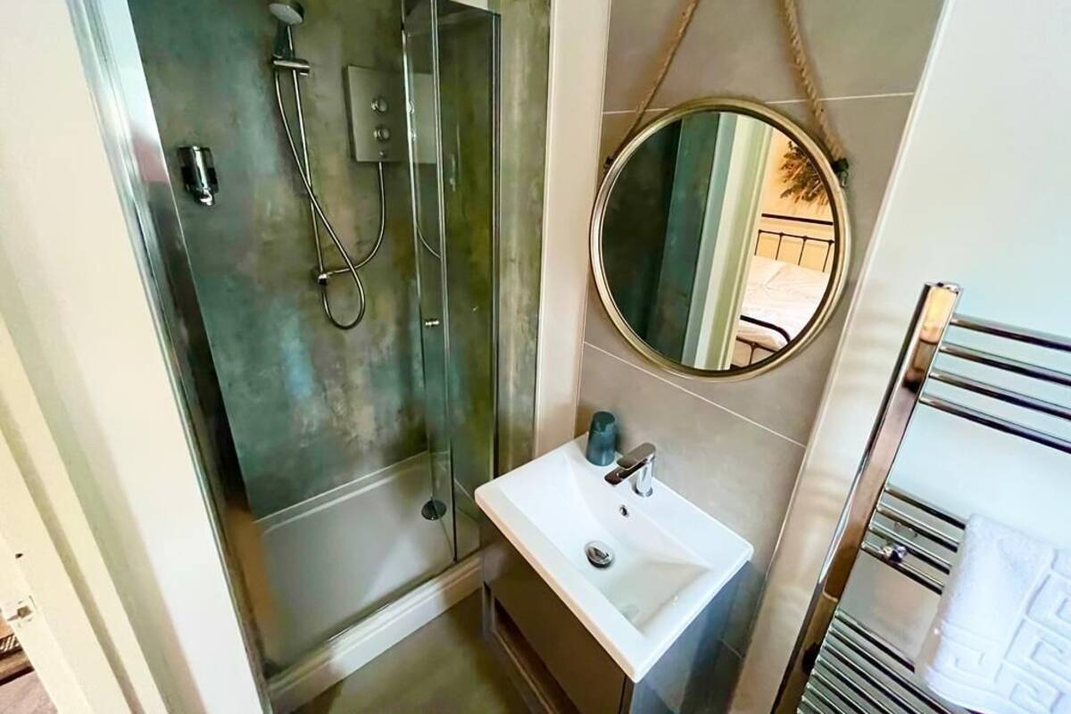 A bathroom with a glass-enclosed shower, a white sink, and a round mirror on the wall.