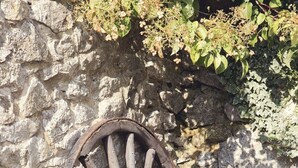 Eine Steinsäule mit einem großen Holzwagen, Blumentöpfe mit bunten Blumen und eine rustikale Gartenlandschaft.