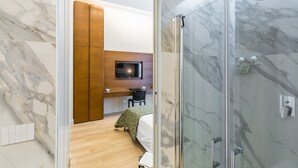 Un bagno moderno con box doccia in vetro, pareti in marmo e un angolo con scrivania in legno e televisore.