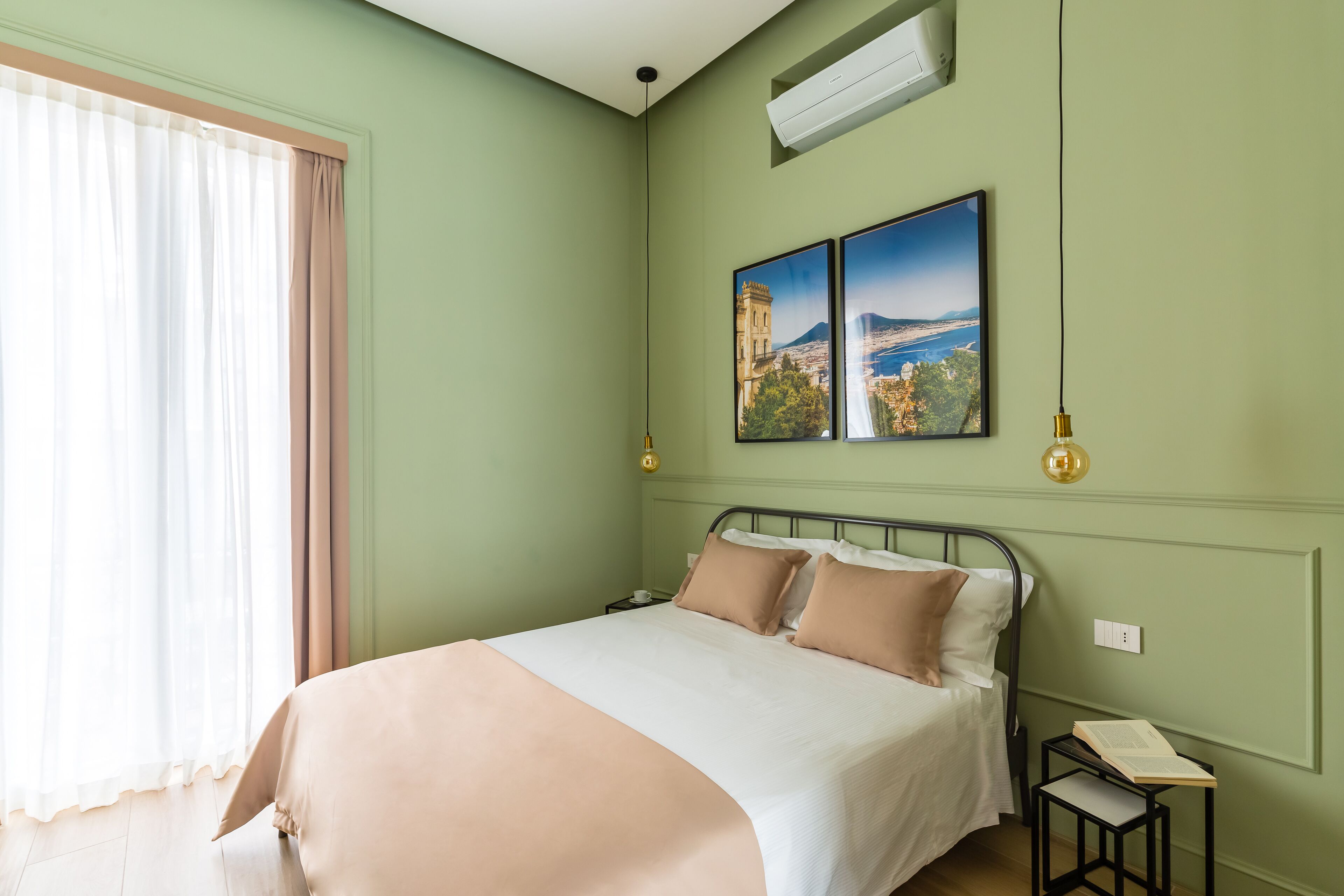 A neatly made bed with a beige and white duvet, a nightstand with a book, and two framed pictures on the wall.