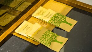 Un plateau en bois contenant plusieurs enveloppes jaunes ornées d’un motif représentant un arbre vert, qui contiennent probablement des articles de toilette ou des informations sur l’hôtel.
